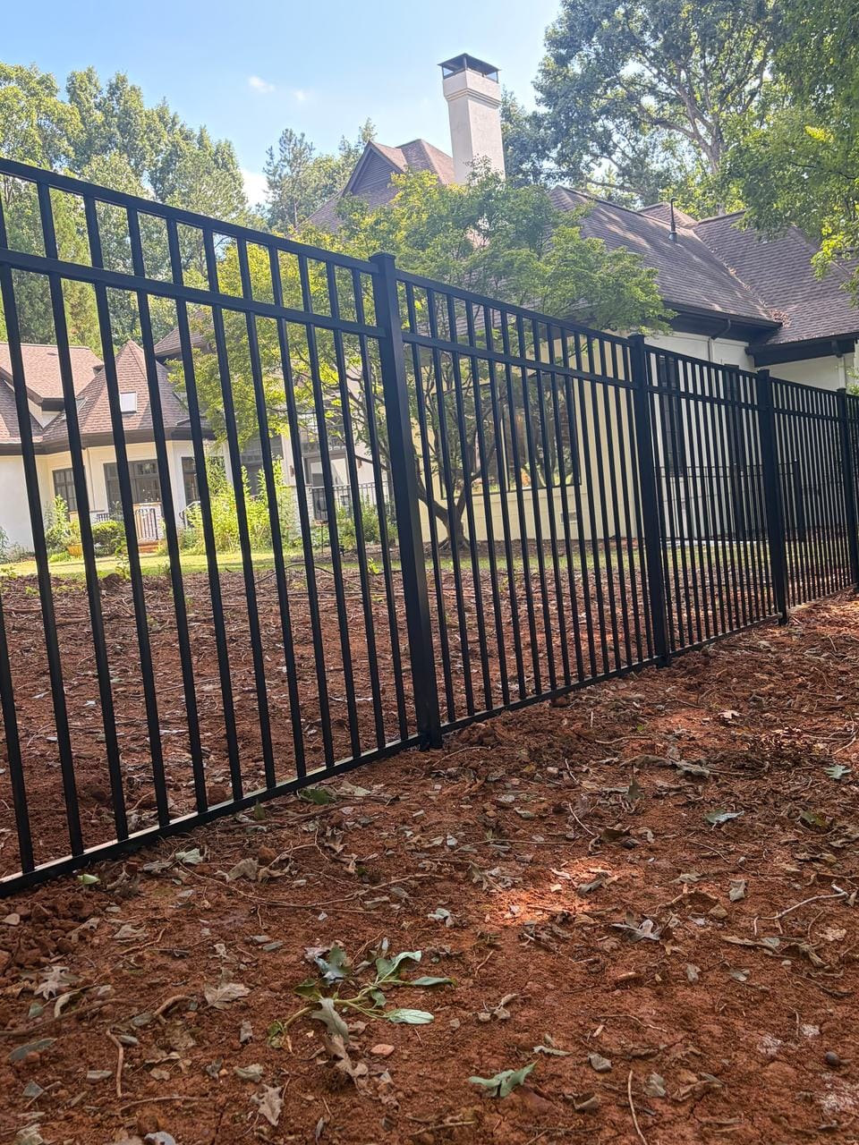 New black aluminum fence on freshly graded red clay behind a house