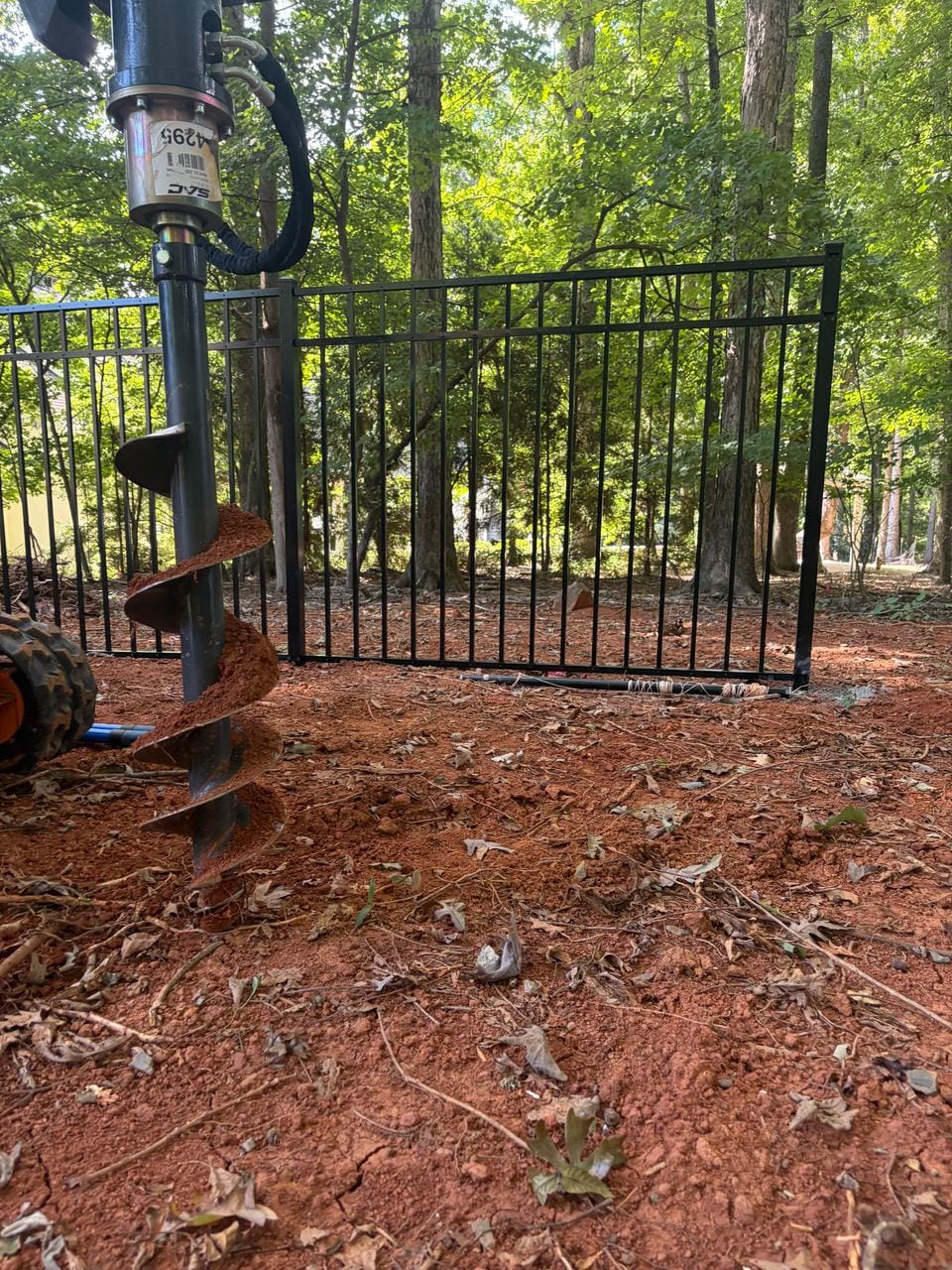 Auger on a compact loader beside a new aluminum fence panel