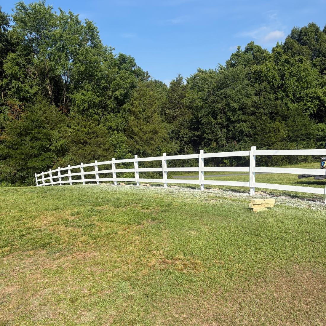 White vinyl three-rail ranch fence across a grassy slope